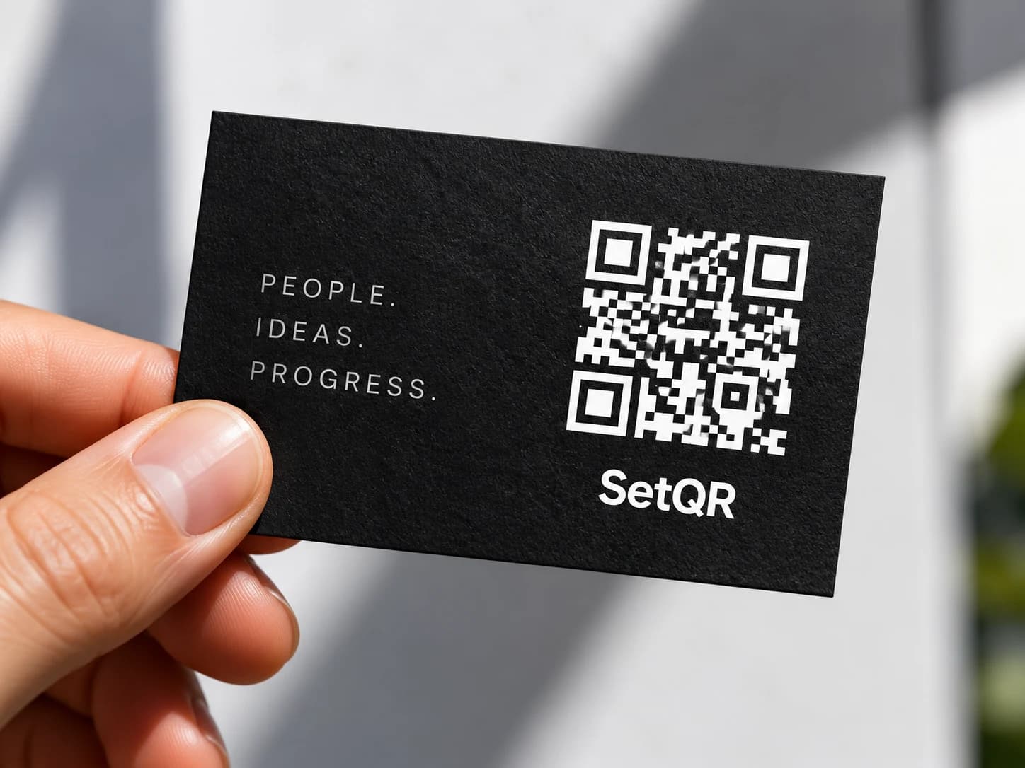 A hand holding a textured black business card with a white QR code.